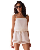 Woman wearing a white lace top and shorts with sunglasses against a peach wall.